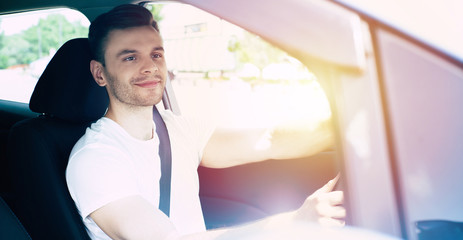 Happy handsome young man driving his car and smiling. Excited driver in urban city. Electro car, vehicle of future.