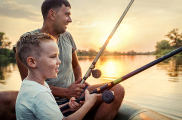 Happy Father and Son together fishing from a boat at sunset time