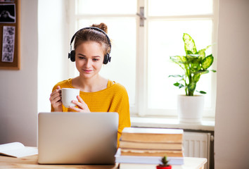 A young female student sitting at the table, using headphones when studying.