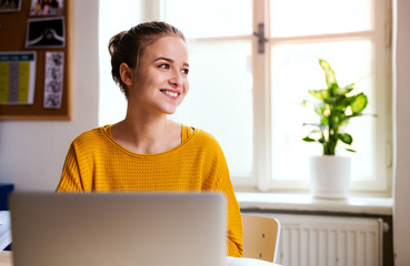 A young female student sitting at the table, using laptop when studying.