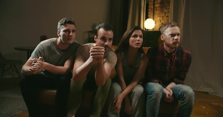 Four friends watch attentively watch movie on TV, follow action, turn heads