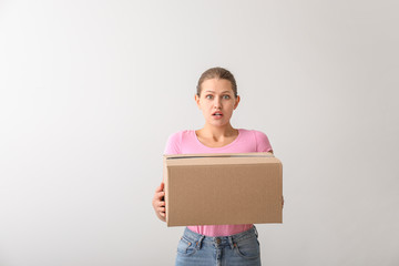 Shocked woman with cardboard box on light background