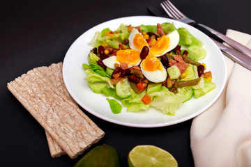 Tuna salad with lettuce, eggs and tomatoes with breads on black table. Diet menu. Top view. Restaurant salad menu concept. Food bloggers background.