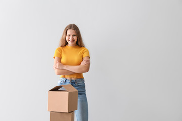 Young woman with cardboard boxes on light background