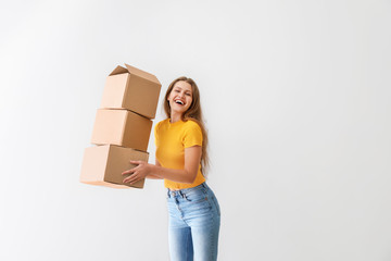 Young woman with cardboard boxes on light background