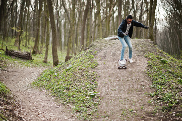 Street style arab man in eyeglasses with longboard on wood.