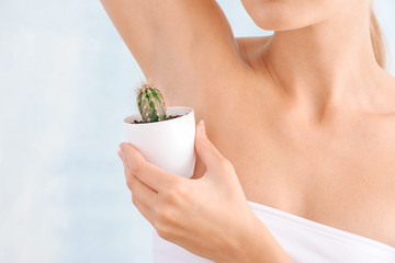 Beautiful young woman with cactus on light background. Depilation concept