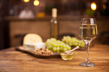 Glass of white wine with super consisting french cheese next to walnuts on rustic wooden table