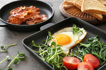 Frying pans with tasty egg and bacon on table