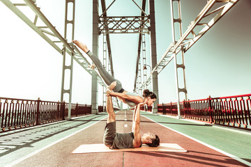 Young couple practicing acroyoga outdoors on the bridge
