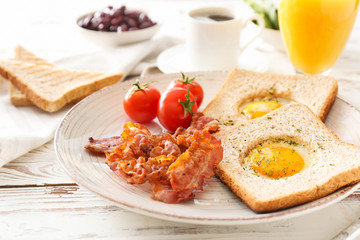 Plate with tasty fried eggs, bacon, toasts and tomato on wooden background