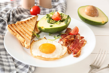 Plate with tasty fried egg, bacon, avocado and toasts on table