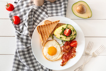 Plate with tasty fried egg, bacon, avocado and toasts on table