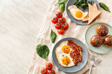 Composition with tasty fried eggs, bacon and buns on table