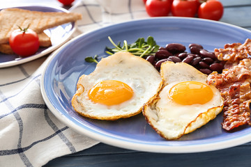 Traditional English breakfast with fried eggs, bacon, beans and toasts on table, closeup