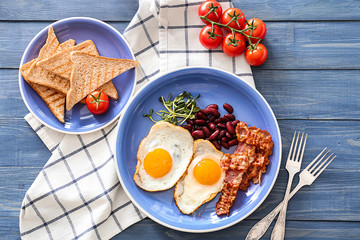 Traditional English breakfast with fried eggs, bacon, beans and toasts on table