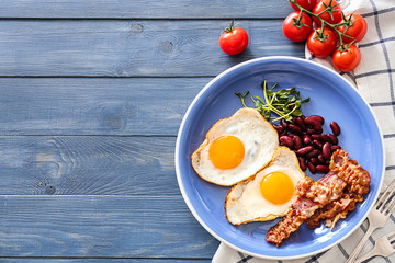 Plate with tasty fried eggs, bacon and beans on table
