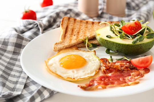 Plate with tasty fried egg, bacon, avocado and toasts on table, closeup