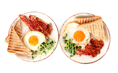 Plates with tasty fried eggs, bacon and toasts on white background