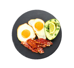 Slate plate with tasty fried eggs, bacon and avocado on white background