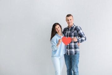 Naklejka premium Adorable loving couple with paper heart on grey background