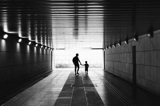 Silhouettes in the tunnel - man and little child walking through empty, dark corridor. Underground passage. Unpleasant, dark place. Kidnapping, stranger, danger, abuse, violence, child safety concept