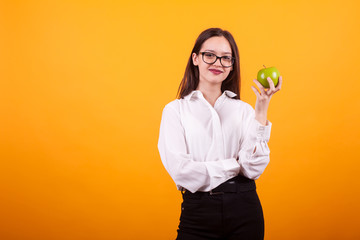 Happy young girl holding a green apple and smiling to the camera over yellow background