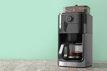 Modern coffee machine on table against color background