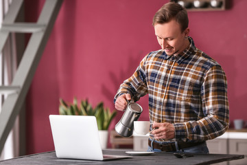 Handsome man with laptop drinking coffee at home