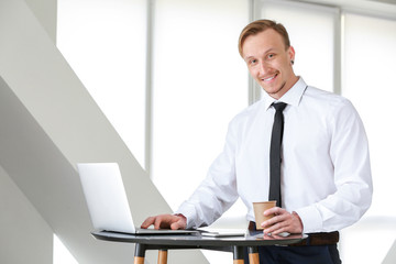 Handsome businessman with laptop drinking coffee in office