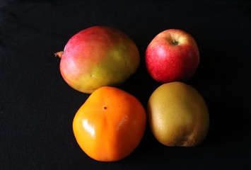 Fototapeta na wymiar Closeup of Tripical fruits, Mango,Apple,Kiwi,Persimmon against black background - tropical still life,Fresh and healthy nutrition.