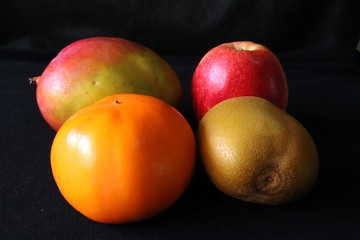 Closeup of Tripical fruits, Mango,Apple,Kiwi,Persimmon against black background - tropical still life,Fresh and healthy nutrition.