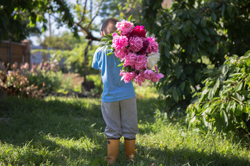 View from the back of little boy in his hands a large bouquet of beautiful peony flowers
