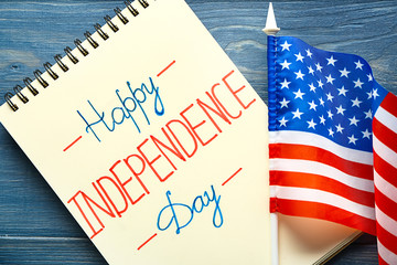 Fototapeta na wymiar Notebook with text HAPPY INDEPENDENCE DAY and USA flag on color wooden background