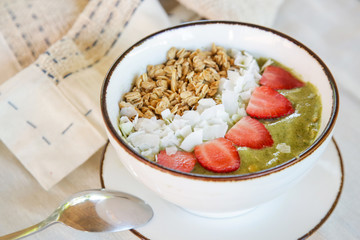 Delicious organic green smoothie bowl garnished with strawberries, sliced almonds and granola