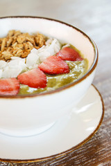 Delicious organic green smoothie bowl garnished with strawberries, sliced almonds and granola