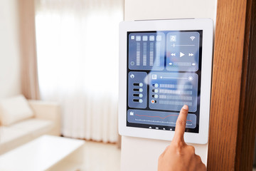 Close-up of woman pointing at display and controlling the light in her apartment with smart home system which hanging on the wall