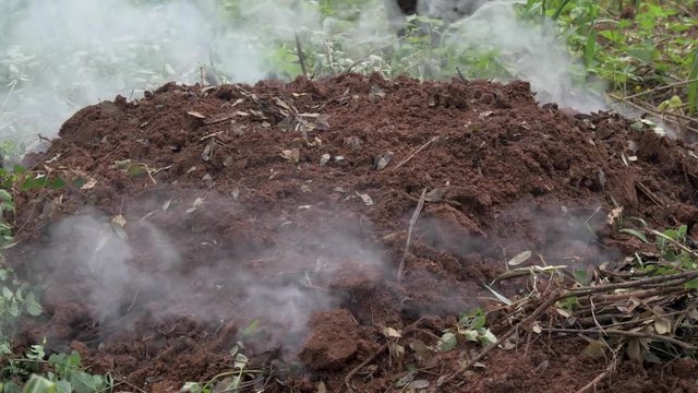 A mound of soil is smoking while charcoal is being made in rural Africa.