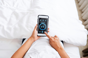 Close-up of woman lying in bed and choosing the normal temperature in bedroom online using smart...
