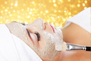 Attractive young woman applying mask on face with brush