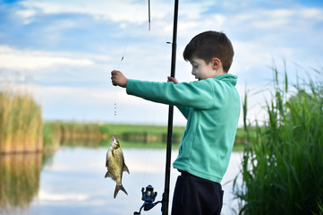 kid boy hold a fish on fishing rod