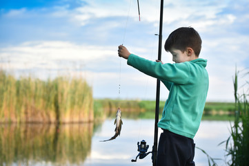 kid boy hold a fish on fishing rod