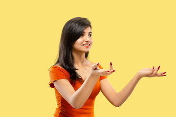Beautiful female half-length portrait isolated on yellow studio background. Young emotional indian woman in dress pointing and showing. Negative space. Facial expression, human emotions concept.