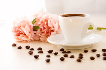 Breakfast in pastel colors. Cup of coffee standing on the table with coffee beans scattered around, against the window and flowers