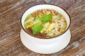 Delicious organic smoothie bowl garnished with pineapple, almond slices and granola, healthy raw vegan meal