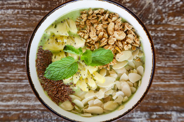 Delicious organic smoothie bowl garnished with pineapple, almond slices and granola, healthy raw vegan meal
