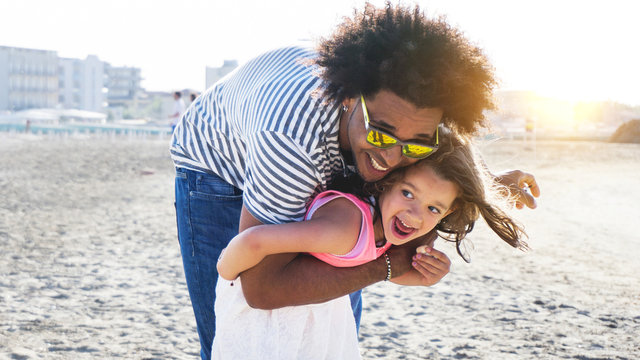 Cute Mixed Race Child Playing With Afro Hair Father On Beach. Concept Of Diversity And Family Fun.