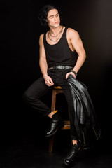 handsome man holding leather jacket and sitting on wooden chair on black