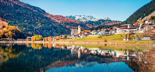 Obraz premium Amazing autumn panorama of Resia village and lake. Amazing morning scene of Italian Alps, South Tyrol, Italy, Europe. Traveling concept background.