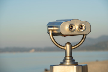 Public binocular on sea shore, close up. Coin operated binocular viewer on blurred background of sunset and sea